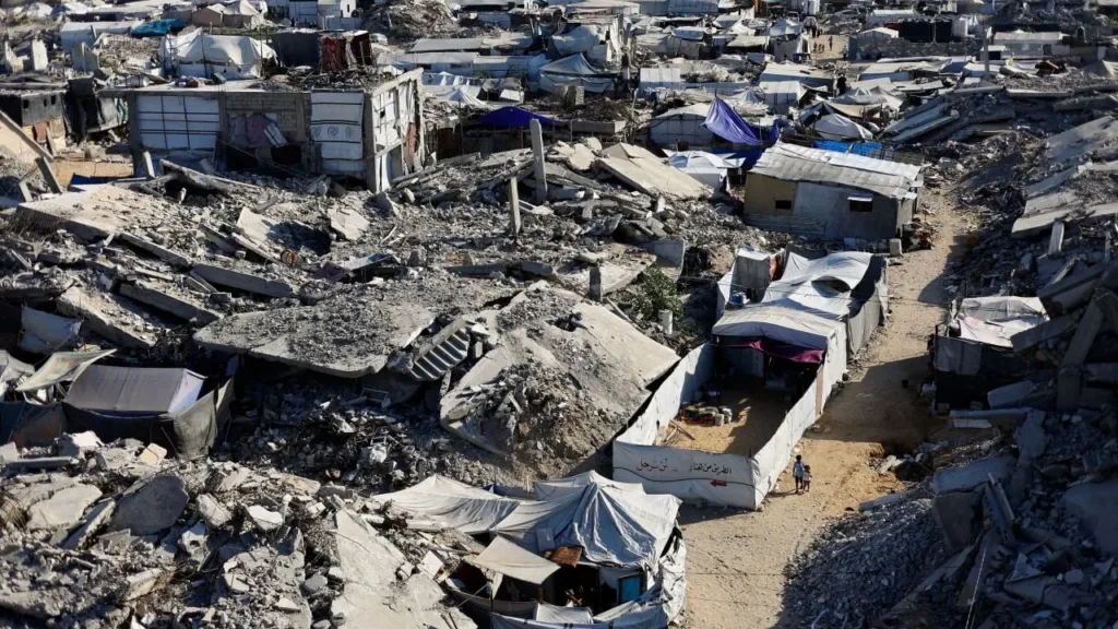 An aerial view shows widespread destruction in Gaza, with sprawling camps of makeshift tents set up among collapsed concrete buildings and rubble.   